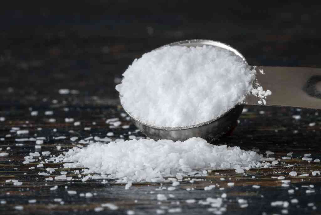 A tablespoon of salt being measured to prepare for aquarium treatment